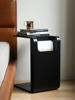 Picture of Black Side Table next to  bed slotted over the seat of a sofa otis side table